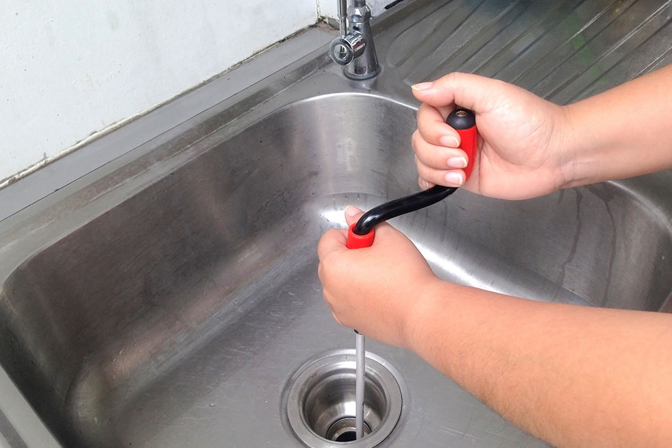 Plumbing using a drain snake to unclog a sink